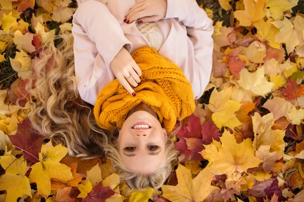 Linda chica rubia está tirada en el parque en la alfombra de hojas de arce amarillo —  Fotos de Stock