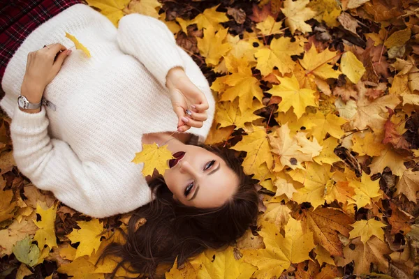 Ziemlich stylische Frau mit modischem Make-up liegt auf Teppich aus gelben Ahornblättern — Stockfoto