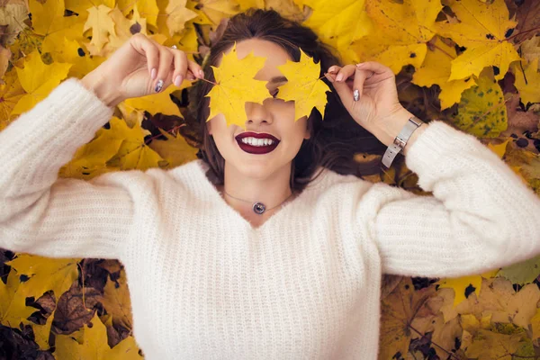 Ziemlich stylische Frau mit modischem Make-up liegt auf Teppich aus gelben Ahornblättern — Stockfoto