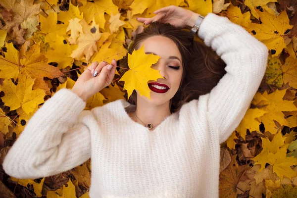 Ziemlich stylische Frau mit modischem Make-up liegt auf Teppich aus gelben Ahornblättern — Stockfoto