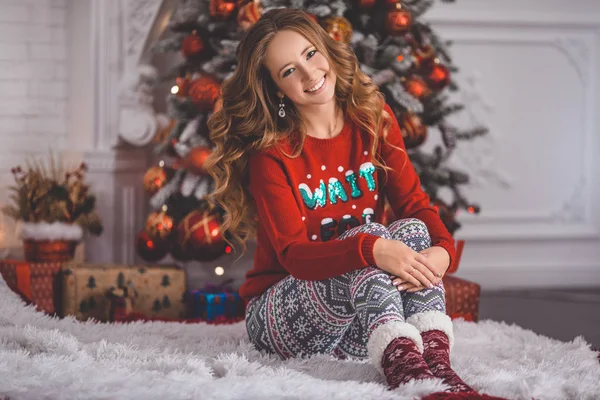 Hermosa chica joven está usando ropa de Navidad acogedora casa sentada cerca del árbol de Navidad —  Fotos de Stock