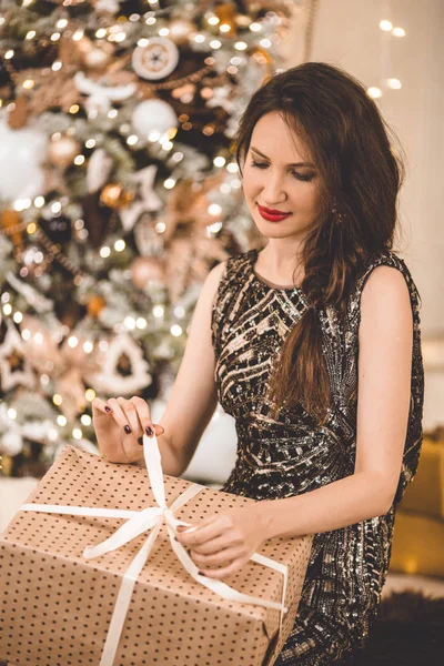 Красивая молодая женщина носит роскошное платье на фоне елки с подарочной коробкой — стоковое фото