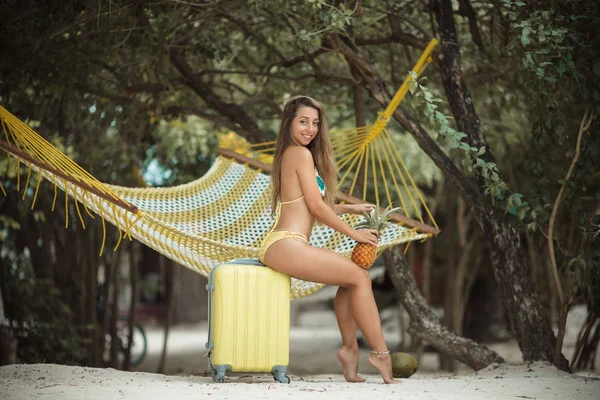 Gyönyörű utazó lány a pihentető a strandon, sárga bőrönd — Stock Fotó