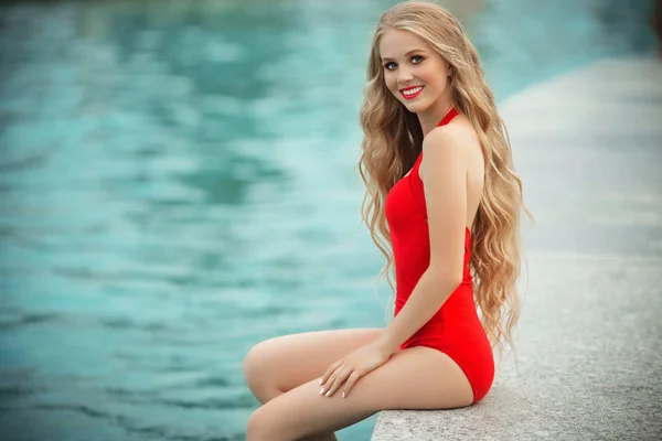 Söt flicka bär röda baddräkt vila nära poolen med blå vatten. sommarsemester — Stockfoto