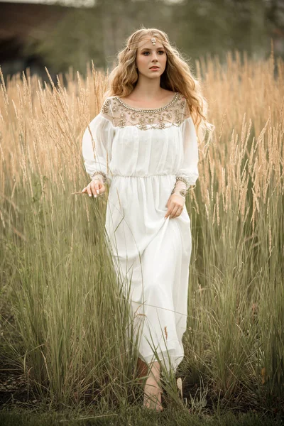 Portrait of happy smiling blonde girl with long blonde hair is wearing white bridal fashion dress on the nature in field of ray — Stock Photo, Image