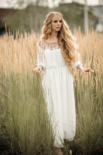Porträtt av glada leende blond flicka med långa blonda hår bär vit brud mode klä på naturen i fältet av ray — Stockfoto