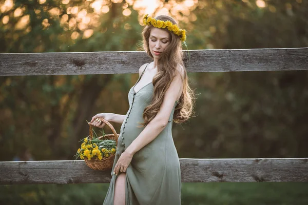 怀孕的漂亮女人是戴着蒲公英花花圈在日落灯, 春天的时间 — 图库照片