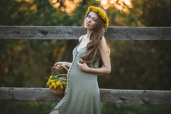 怀孕的漂亮女人是戴着黄色蒲公英花花圈在日落灯, 春天的时间 — 图库照片