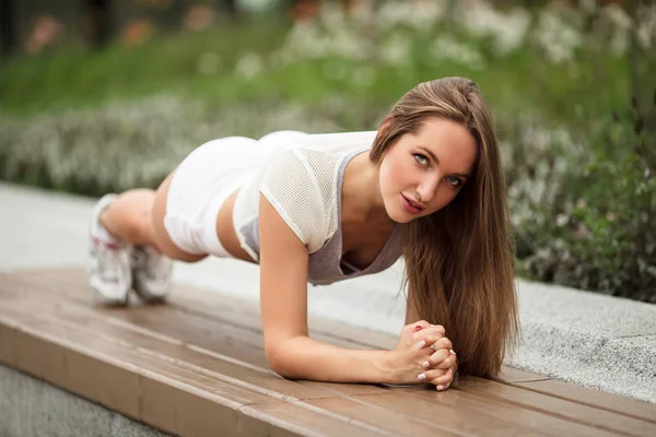 Joven hermosa chica haciendo ejercicios de tablón en el parque verde de la ciudad —  Fotos de Stock