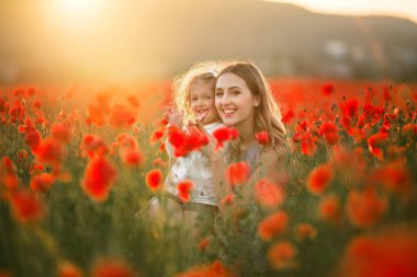 Genç anne ile kız güzel gülümseyen çocuk üzerinde günbatımı ışıkları haşhaş çiçekleri alanında eğlenceli yaşıyorsanız