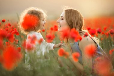 Genç anne ile kız güzel gülümseyen çocuk üzerinde günbatımı ışıkları haşhaş çiçekleri alanında eğlenceli yaşıyorsanız
