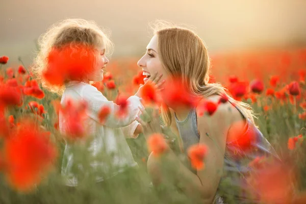 Vackra leende barn flicka med ung mamma har roligt i fält av vallmo blommor över solnedgången ljus — Stockfoto