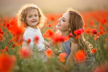 Anne ile kız güzel gülümseyen çocuk üzerinde günbatımı ışıkları kırmızı haşhaş çiçekleri alanında eğlenceli yaşıyorsanız