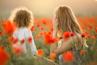 Anne ile kız güzel gülümseyen çocuk üzerinde günbatımı ışıkları kırmızı haşhaş çiçekleri alanında eğlenceli yaşıyorsanız