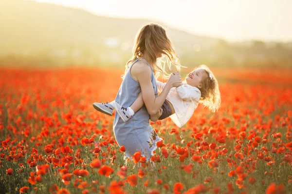 Frumoasă fată zâmbitoare copil cu mama se distrează în domeniul de flori de mac roșu peste lumini de apus de soare, timp de primăvară — Fotografie, imagine de stoc