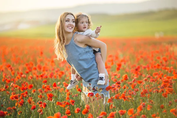 Bela menina sorridente com a mãe estão se divertindo no campo de flores de papoula vermelha sobre luzes de pôr do sol, tempo de primavera — Fotografia de Stock