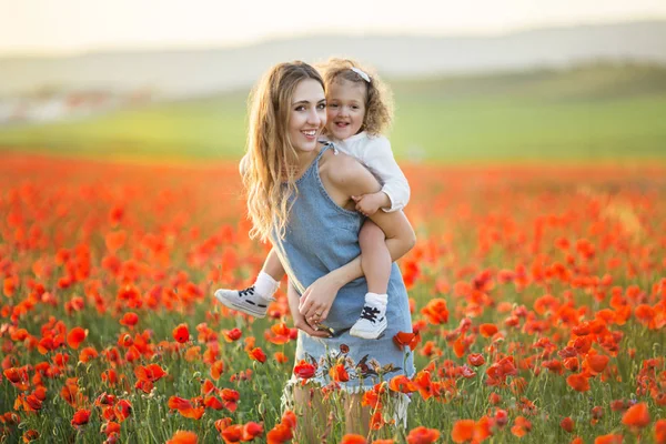 Красива усміхнена дівчинка з матір'ю розважається в полі червоних макових квітів над заходом сонця, весняний час — стокове фото