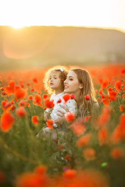 Beautiful smiling baby girl with mother are having fun in field of red poppy flowers over sunset lights, spring time — Stock Photo, Image