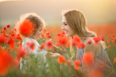 Genç anne ile kız güzel gülümseyen çocuk üzerinde günbatımı ışıkları haşhaş çiçekleri alanında eğlenceli yaşıyorsanız