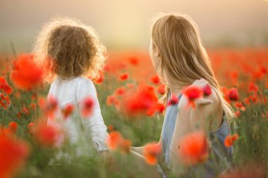 Anne ile kız güzel gülümseyen çocuk üzerinde günbatımı ışıkları kırmızı haşhaş çiçekleri alanında eğlenceli yaşıyorsanız
