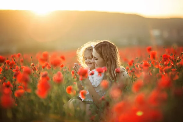 Belle fille enfant avec jeune mère portent des vêtements décontractés dans le domaine des fleurs de pavot sur les lumières du coucher du soleil — Photo