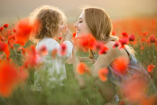 Krásná dívka s úsměvem dítěte s matkou se baví v oblasti červené květy máku nad slunce světla — Stock fotografie