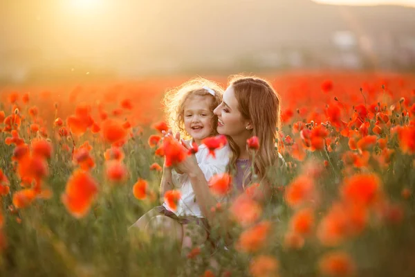 Belle petite fille souriante avec mère s'amusent dans le domaine des fleurs de pavot rouge sur les lumières du coucher du soleil, le printemps — Photo