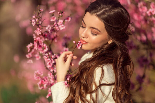 Portrait of young beautiful girl posing near blossom tree with pink flowers.