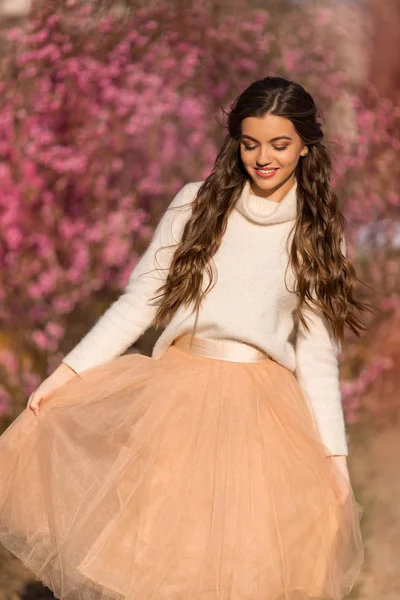 Ritratto di giovane bella ragazza con pelle perfetta indossa vestiti romantici posa vicino albero di fiori in giardino ciliegio — Foto Stock