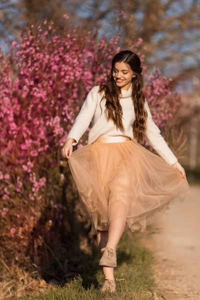 Молодая красивая девушка-подросток с идеальной кожей носит романтическую одежду, позируя возле цветущего дерева в вишневом саду — стоковое фото