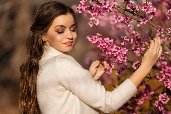 完璧な肌とメイクを持つ若い美しい十代の少女は、桜の庭のブロッサムツリーの近くにポーズロマンチックな服を着ています — ストック写真