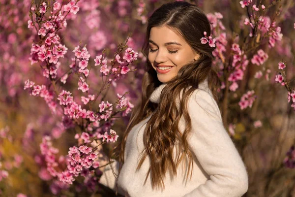 Joven hermosa adolescente con la piel perfecta y maquillaje está usando ropa romántica posando cerca del árbol de flores en el jardín de cerezos —  Fotos de Stock
