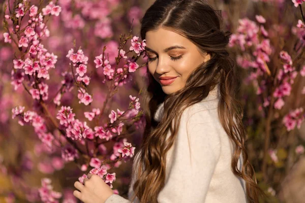 Ung vacker tonåring flicka med perfekt hud och makeup är klädd i romantiska kläder poserar nära blomma träd i körsbärs trädgård — Stockfoto