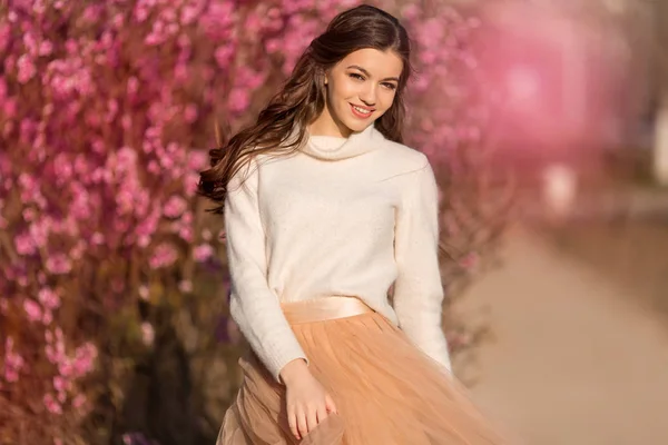 Lycklig vacker tonåring flicka med perfekt hud och makeup är klädd i romantiska kläder poserar nära blomma träd i körsbärs trädgård — Stockfoto