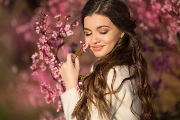 Hübsches lächelndes Teenie-Mädchen posiert in der Nähe von Blütenbaum mit rosa Blumen. — Stockfoto