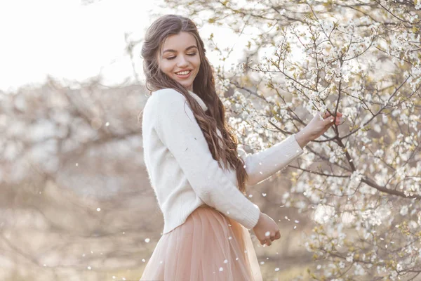 Pretty smiling teen girl are posing in garden near blossom cherry tree with white flowers. Spring time — Stock Photo, Image