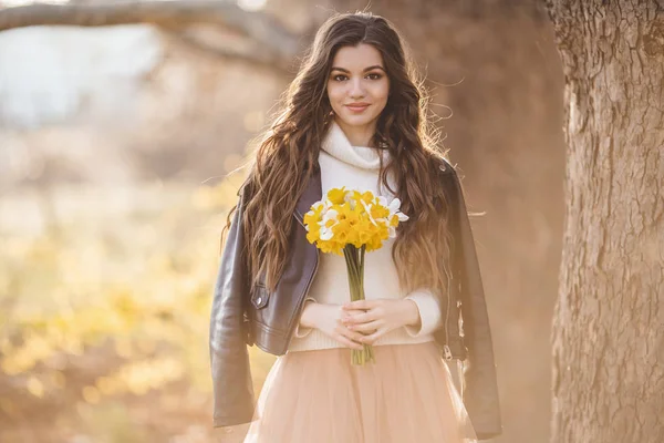 Pretty smiling teen girl are holding bouquet of narcissus flowers over sunset lights. Spring time