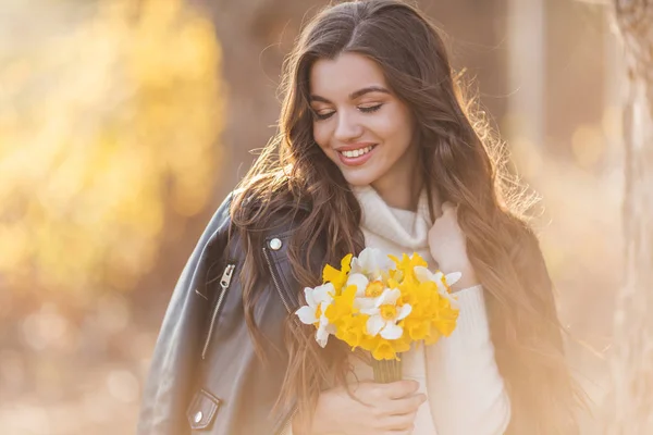 Porträtt av leende tonåring flicka håller bukett Narcissus blommor i parken över solnedgången ljus. Vårtid — Stockfoto