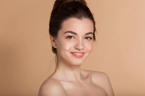 Beautiful face portrait of young woman with cosmetic cream on a cheek. Skin care and health concept. — Stock Photo, Image