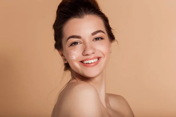 Hermoso retrato facial de una joven sonriente con crema cosmética en la mejilla. Cuidado de la piel y concepto de salud . — Foto de Stock