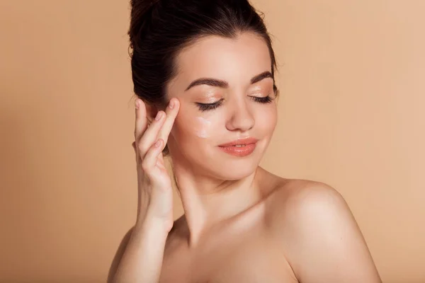 Il bel ritratto di faccia di giovane donna sta applicando la crema per il viso a una guancia. Cura della pelle e concetto di salute . — Foto Stock