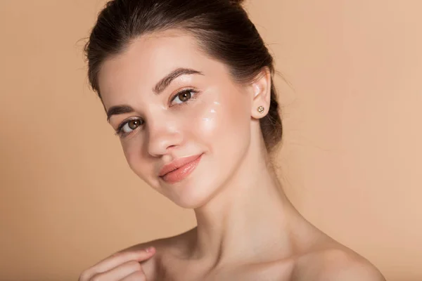 Retrato de cara bonito de mulher jovem com pele perfeita com creme de cara hidratante em uma bochecha. Cuidados com a pele e conceito de saúde . — Fotografia de Stock