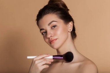 Mükemmel bir cilde sahip güzel kızın closeup portre elinde makyaj fırçası tutuyor. Bej üzerinde izole edilmiş. Güzellik ve kozmetik konsepti.