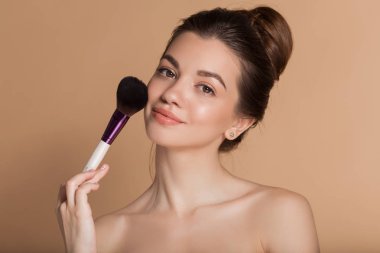 Mükemmel bir cilde sahip güzel mutlu genç kızın closeup portresi elinde makyaj fırçası tutuyor. Bej üzerinde izole edilmiş. Güzellik ve kozmetik konsepti.