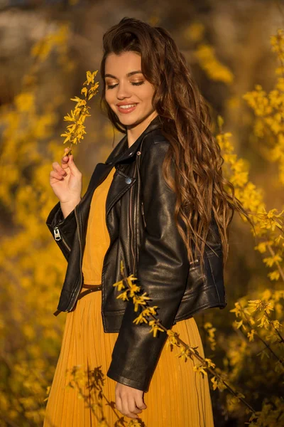 Portrait pretty teenager girl with long hair is near aroma bushes with yellow flowers. Spring time. — Stock Photo, Image