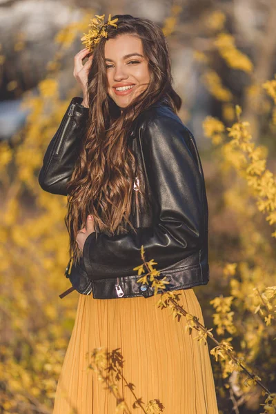 Porträtt ganska tonårs flicka med långt hår är nära arom buskar med gula blommor. Vårtid. — Stockfoto