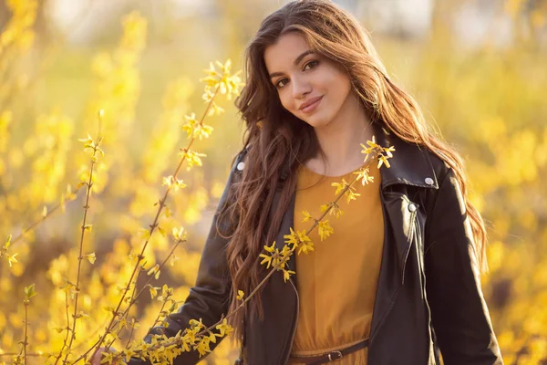 Portrait pretty teen girl with long hair is near aroma bushes with yellow flowers. Spring time. — Stock Photo, Image