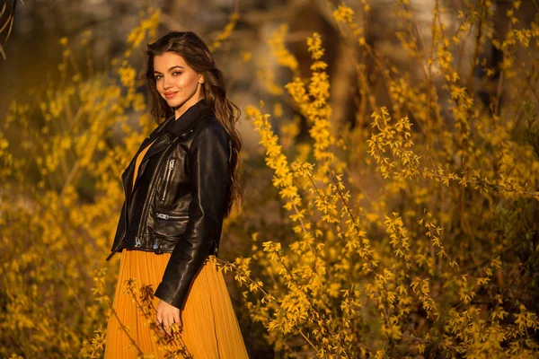 Porträtt av leende tonåring flicka med långt hår är nära buskar med gula blommor. Vårtid. — Stockfoto