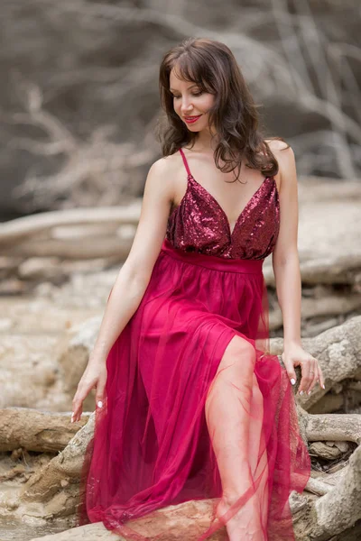 Mladá krásná žena má na sobě módní červené šaty sedí v blízkosti vodopádu — Stock fotografie