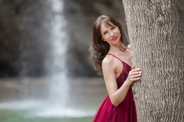 Portrait de jeune belle femme porte une robe rouge mode marchant dans la forêt près de la cascade — Photo